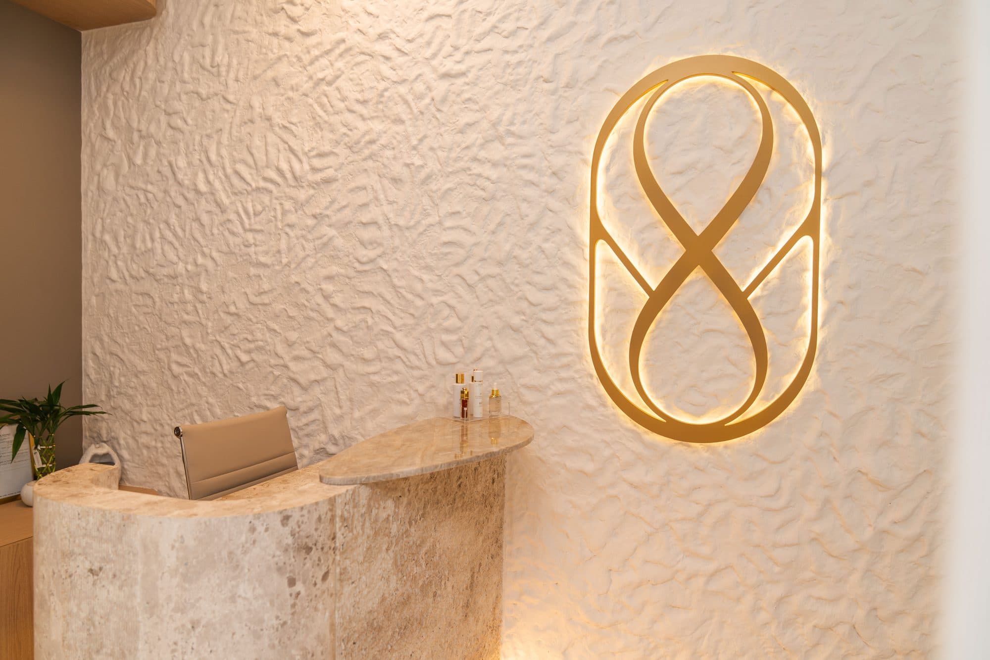 Balcão de travertino da recepção, diante do monograma iluminado