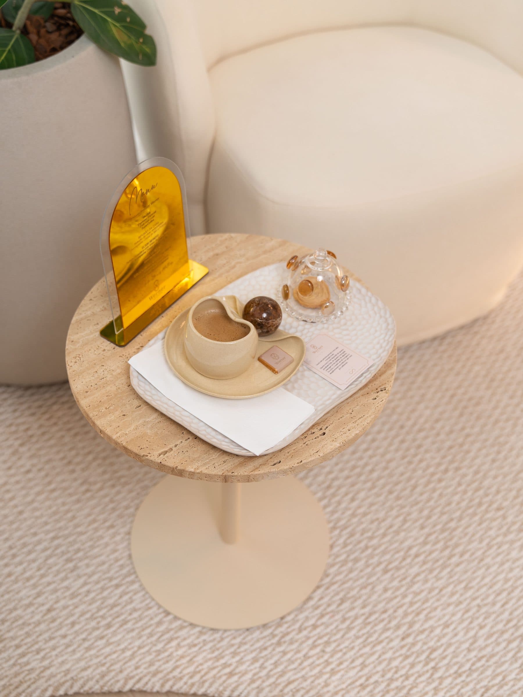 Mesa lateral com café, doce e menu de bebidas ao lado de uma poltrona da sala de espera